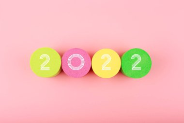 Parlak pembe arkaplanın ortasındaki renkli dairelerde 2022 numara. Yeni Yıl Asgari Moda Konsepti 