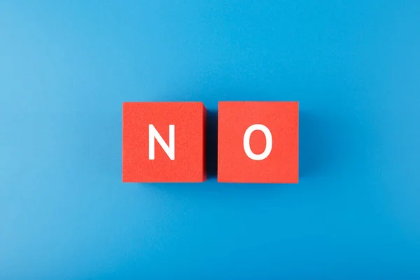 Flat lay with single word no on red cubes against blue background. Say no to violence, toxic people, discrimination, agism and other negative factors