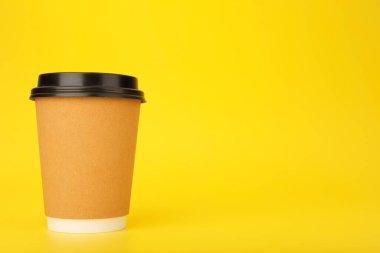 Kahverengi karton bardakta çay ya da fotokopi alanı olan parlak sarı arka planda kahve. Sıcak içecek konsepti.