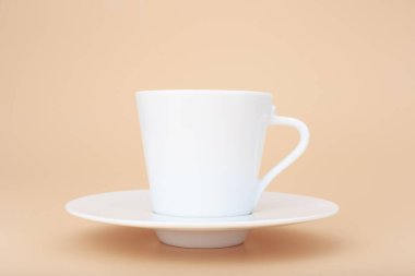 Beyaz seramik kahve fincanı ve çay tabağı ile pastel bej arka plan ve fotokopi alanı. Sıcak içecekler, seramik bardaklar ve mutfak aletleri kavramı