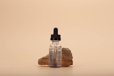 Doğal taşın yanında deri serumu şişesi ve fotokopi alanı olan parlak bej arka plan. Yaşlanmaya karşı günlük tedavi için lüks cilt serumu veya yağ kavramı