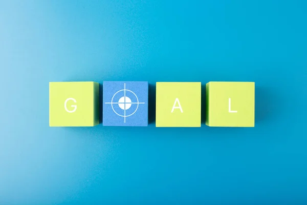 Goal single word and target symbol written on green and yellow geometric figures in a row on blue background Stock Obrázky