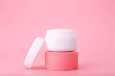 Pembe kaide üzerine açık kozmetik kavanozu parlak pembe arka plana karşı. Besleyici kremi tamir etme konsepti 