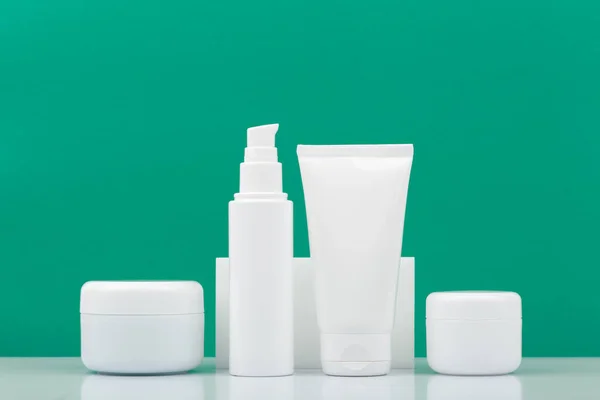 Set of cosmetic products for daily skincare in a row on white table against green background Fotografia De Stock
