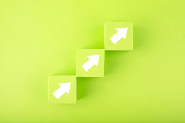 Ladder career, sales or business growth path concept. Green toy cubes as step stairs with white arrows up 