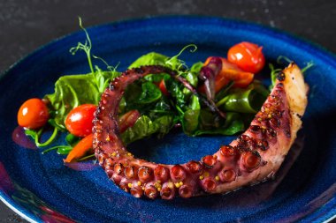 fried octopus with tomatoes and herbs on a blue plate