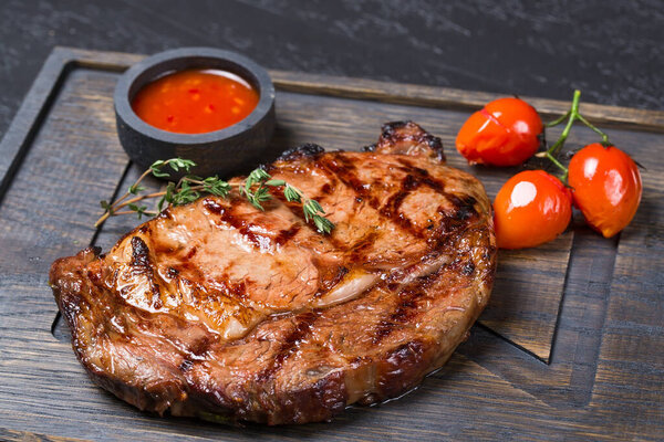 Fried Rib Eye steak with cherry tomatoes and sauce on a wooden board
