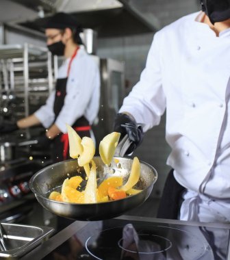 Genç erkek aşçı, ticari mutfakta sebze çeviriyor.