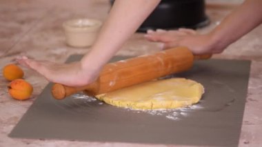 Close up of woman rolling dough with rolling pin on kitchen table.