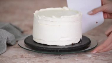 Kadınların elleri sünger katlı kekin üzerine krem şanti sürüyor..