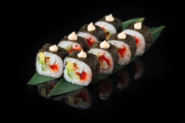 Siyah bir arka planda yansımalı geleneksel lezzetli suşi rulosu. Pilavlı suşi, nori, krem peynir, tobiko havyarı, avokado. Suşi menüsü. Japon mutfağı, restoran. Asya yemekleri