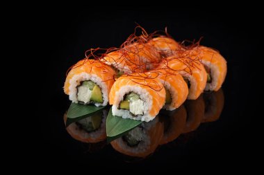 Siyah bir arka planda yansımalı geleneksel lezzetli suşi rulosu. Pilavlı suşi, nori, krem peynir, tobiko havyarı, avokado. Suşi menüsü. Japon mutfağı, restoran. Asya yemekleri
