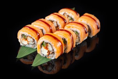 Siyah bir arka planda yansımalı geleneksel lezzetli suşi rulosu. Pilavlı suşi, nori, krem peynir, tobiko havyarı, avokado. Suşi menüsü. Japon mutfağı, restoran. Asya yemekleri