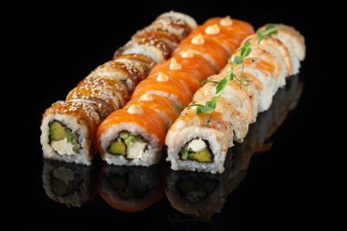 Siyah bir arka planda yansımalı geleneksel lezzetli suşi rulosu. Pilavlı suşi, nori, krem peynir, tobiko havyarı, avokado. Suşi menüsü. Japon mutfağı, restoran. Asya yemekleri