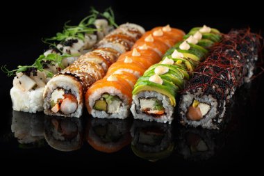 Siyah bir arka planda yansımalı geleneksel lezzetli suşi rulosu. Pilavlı suşi, nori, krem peynir, tobiko havyarı, avokado. Suşi menüsü. Japon mutfağı, restoran. Asya yemekleri