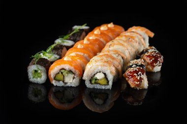 Siyah bir arka planda yansımalı geleneksel lezzetli suşi rulosu. Pilavlı suşi, nori, krem peynir, tobiko havyarı, avokado. Suşi menüsü. Japon mutfağı, restoran. Asya yemekleri