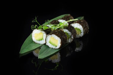 Siyah bir arka planda yansımalı geleneksel lezzetli suşi rulosu. Pilavlı suşi, nori, krem peynir, tobiko havyarı, avokado. Suşi menüsü. Japon mutfağı, restoran. Asya yemekleri