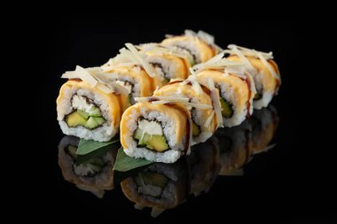 Siyah bir arka planda yansımalı geleneksel lezzetli suşi rulosu. Pilavlı suşi, nori, krem peynir, tobiko havyarı, avokado. Suşi menüsü. Japon mutfağı, restoran. Asya yemekleri