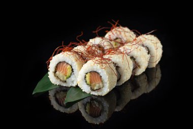Siyah bir arka planda yansımalı geleneksel lezzetli suşi rulosu. Pilavlı suşi, nori, krem peynir, tobiko havyarı, avokado. Suşi menüsü. Japon mutfağı, restoran. Asya yemekleri