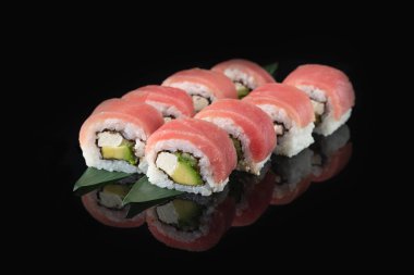 Siyah bir arka planda yansımalı geleneksel lezzetli suşi rulosu. Pilavlı suşi, ton balığı, nori, krem peynir, avokado. Suşi menüsü. Japon mutfağı, restoran. Asya yemekleri