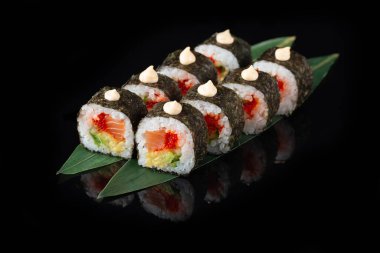 Siyah bir arka planda yansımalı geleneksel lezzetli suşi rulosu. Pilavlı suşi, nori, krem peynir, tobiko havyarı, avokado. Suşi menüsü. Japon mutfağı, restoran. Asya yemekleri