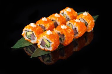 Siyah bir arka planda yansımalı geleneksel lezzetli suşi rulosu. Pilavlı suşi, nori, krem peynir, tobiko havyarı, avokado. Suşi menüsü. Japon mutfağı, restoran. Asya yemekleri