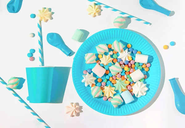 Creative layout made of blue paper glasses with straws, dishes, meringues and balloons on white background. Festive concept. Birthday and party theme.