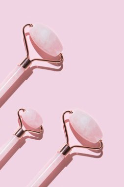 Pastel pembe güneşli arka planda pembe kuvars yüz silindirlerinden oluşan yaratıcı bir düzen. Asgari düzeyde. Cilt bakımı ve güzellik anlayışı. Üst Manzara. Düz yatıyordu