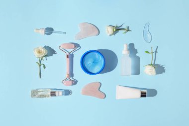 Kolajen göz bantlarından, yüz silindiri ve gua sha masajcılarından, mavi pastel arka planda gerekli yağlardan ve serumdan oluşan yaratıcı bir kompozisyon. Doğal tedavi konsepti. Üst Manzara. Düz yatıyordu