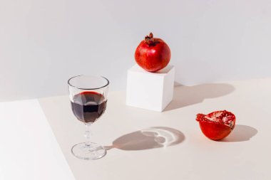 Kırmızı şaraptan ya da meyve suyundan yapılmış yaratıcı bir kompozisyon ya da güneş ışığıyla kaplanmış pastel arka planda duran nar. Yaz tatili konsepti. Asgari biçim.