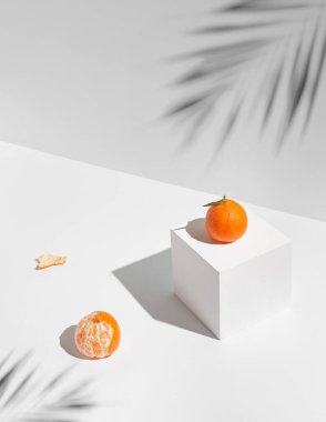 Gölgeler ve geometrik küple beyaz güneş ışığıyla aydınlatılmış taze mandalina meyvelerinden oluşan yaratıcı bir kompozisyon. Sağlıklı yiyecekler ve yaz içeceği konsepti. Asgari biçim.