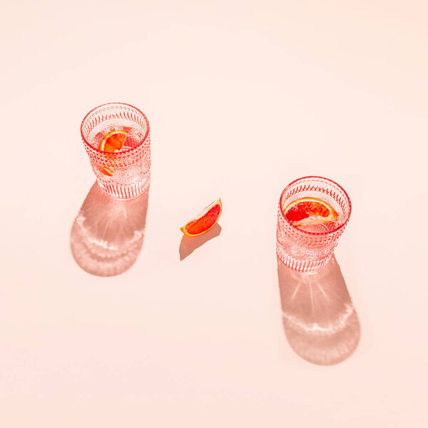 Creative composition made of two glasse with cocktail or lemonade on beige pastel background with lobule of bloody orange. Summer refreshment concept. Sunlit flat lay. Minimal style. Top view