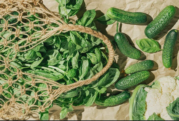 Creative layout made of fresh basil and cucumbers in mesh bag on craft papar background with cauliflower. Healthy food ingredient concept.