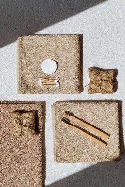 Creative layout made of toothbrush, natural soap and cootton pads on sunlit background with towels. Morning routine concept. Top view. Flat lay