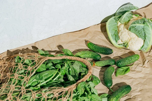 Creative layout made of fresh basil and cucumbers in mesh bag on craft papar background with cauliflower. Healthy food ingredient concept.