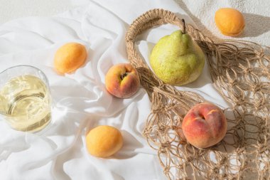 Creative composition made of fruits, glass of lemonede or cocktail and mesh bag on white fabric. Summer refreshment and freshness background. Vegan and vegetarian food concept. Zero west theme.