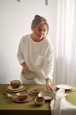 Pijamalı genç kız masayı hazırlıyor. Doğal kumaşlar ve malzemeler var. Konforlu ev.