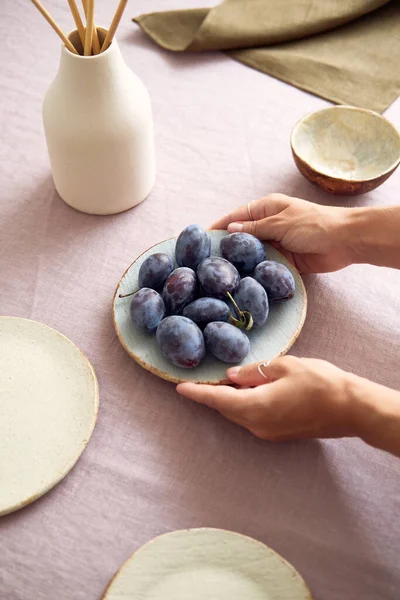 Prugne dolci succose fresche su un piatto di argilla insolito. La ragazza serve il tavolo. — Foto Stock