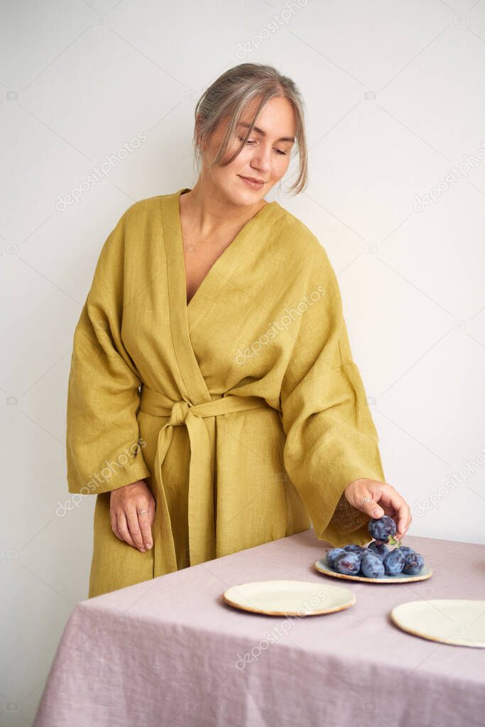 Young girl in a dressing gown lays the table. Natural fabrics and materials around. Cozy home.