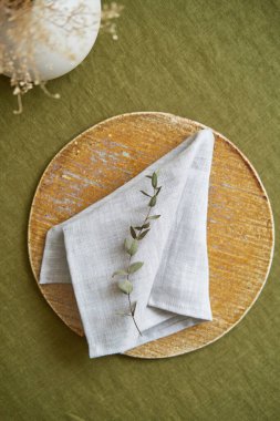 Masa ayarlama seçeneği. Bir keten gri peçete kahverengi bir tabakta düzgünce katlanır. Zeytin arkaplanı.