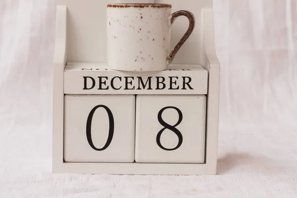 December 8th. Day 8 of month, calendar and a cup of coffee or tea on white background.  White block calendar present date 08 and month December. Empty space for text
