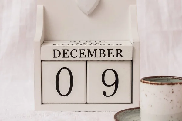 December 9th. Day 9 of month, calendar and a cup of coffee or tea on white background.  White block calendar present date 09 and month December. Empty space for text