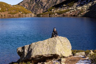 Bir çocuk bir dağ gölünün kıyısında büyük bir taşın üzerinde oturuyor. Rybka Gölü. Dukkin Gölleri. Arkhyz. Karachay-Çerkessia. Rusya.