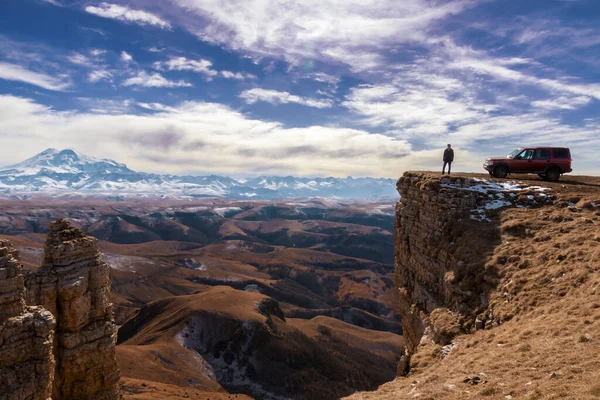 Sonbaharda Bermamyt Platosu 'ndan Elbrus Dağı' nın manzarası. Bir araba ve bir adamın siluetinin yanında..