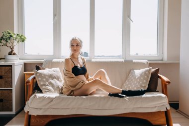 Hamile kadın evdeki pencerenin kenarında, yumuşak bir ışıkta kanepede oturuyor..