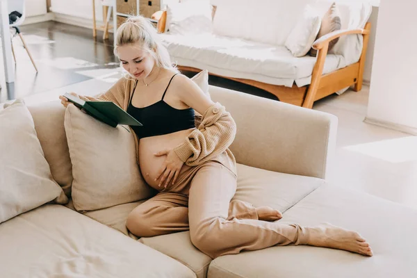 Blondynka Ciąży Ubrana Strój Domowy Siedząca Kanapie Domu Czytająca Książkę — Zdjęcie stockowe