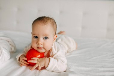 Beş aylık bebek karnının üstüne yatmış, gülümsüyor, kırmızı bir topla poz veriyor..