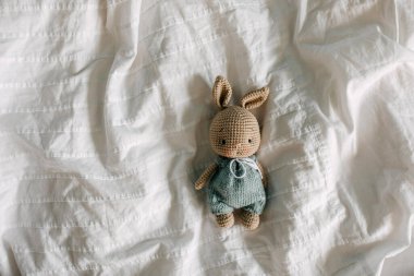 Örülmüş el yapımı tavşan oyuncağı. Beyaz çarşafın üzerinde yeşil bir tulum içinde..