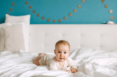 Beş aylık bebek beyaz çarşafın üzerinde karnı üzerinde uzanmış, gülümsüyor ve kameraya bakıyor..