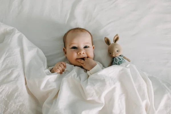 Щаслива Дитина Лежить Ліжку Під Білою Якою Ковдрою Посміхаючись Смоктати — стокове фото